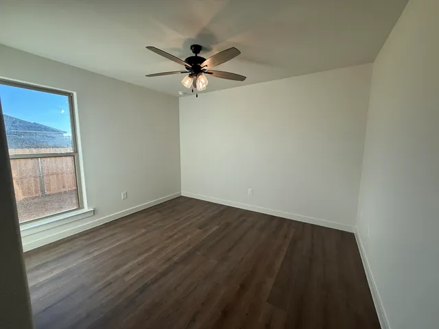 an empty room with wooden floor fan and windows
