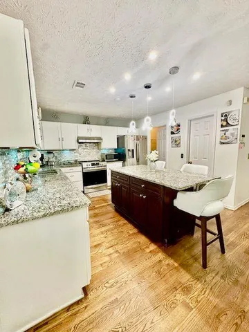 a large kitchen with kitchen island granite countertop wooden cabinets a stove a sink and a dining table