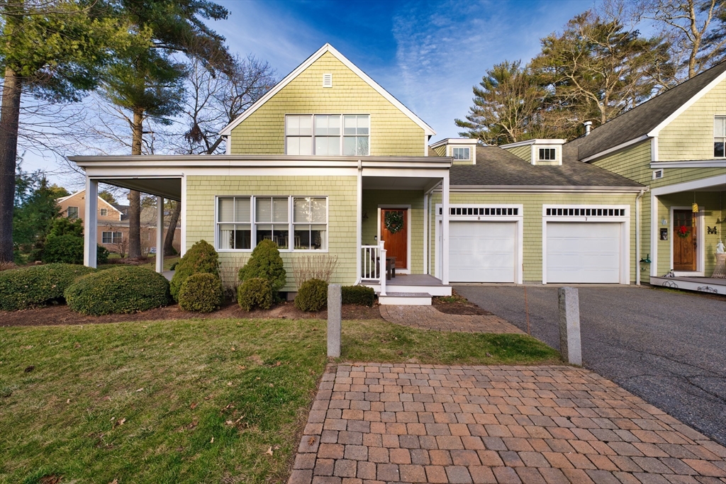 a view of a brick house with a yard plants and large tree