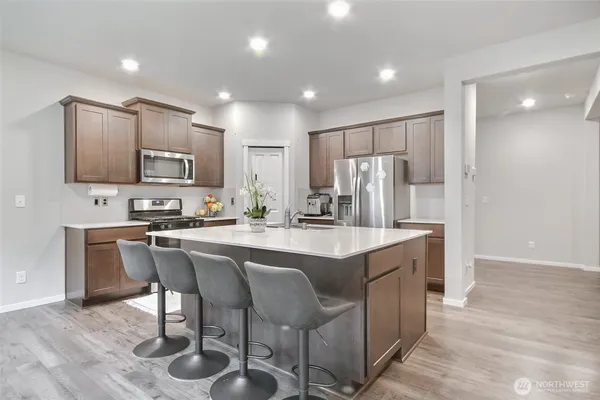 a kitchen with stainless steel appliances granite countertop a sink a stove a refrigerator cabinets and chairs