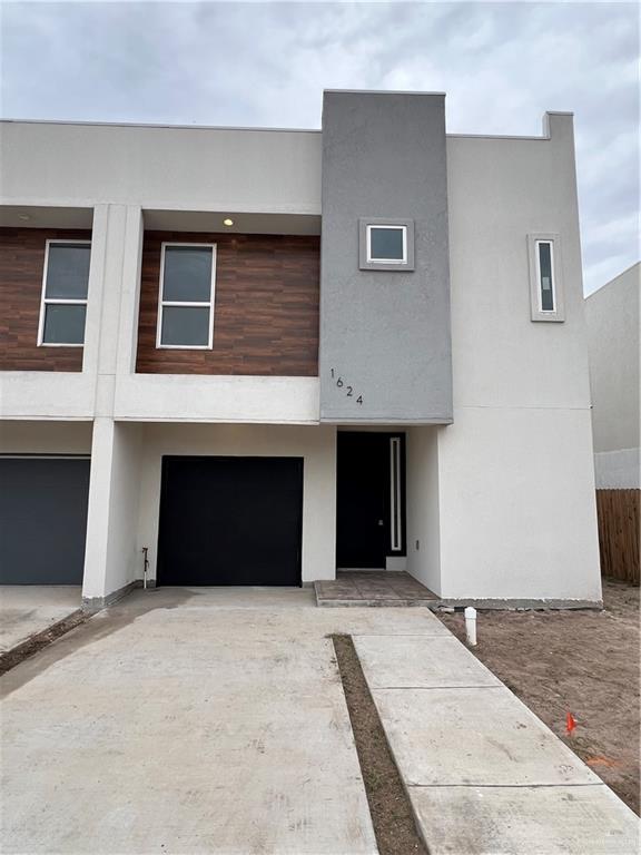 View of front of home featuring a garage, fence, concrete driveway, and stucco siding