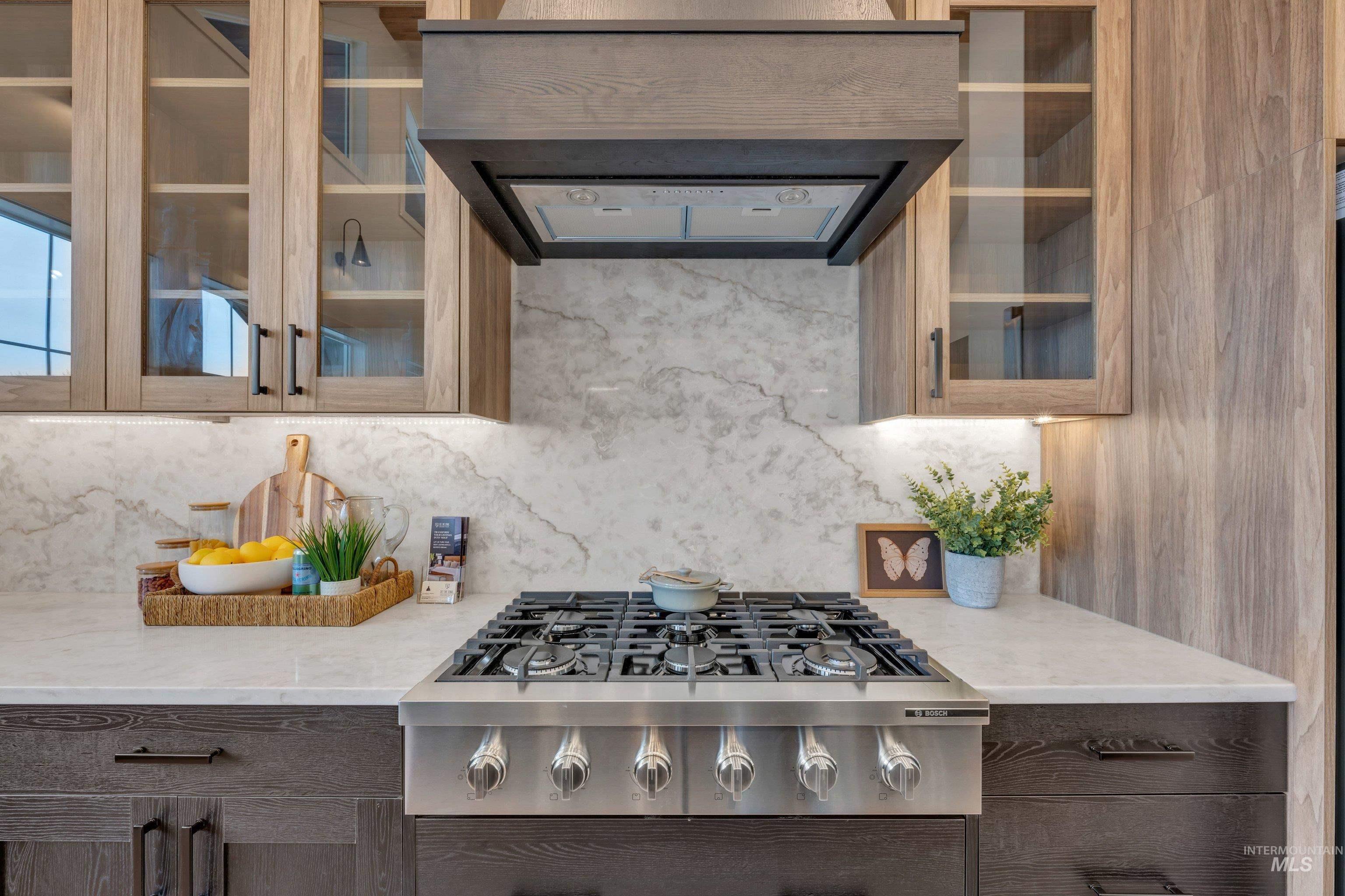 24871 Ardmore Court Caldwell, ID 83607 - Photo 12 of 44 Kitchen with glass fronted cabinets, stainless steel gas stovetop, range hood, light stone counters, and dark wood finish cabinetry