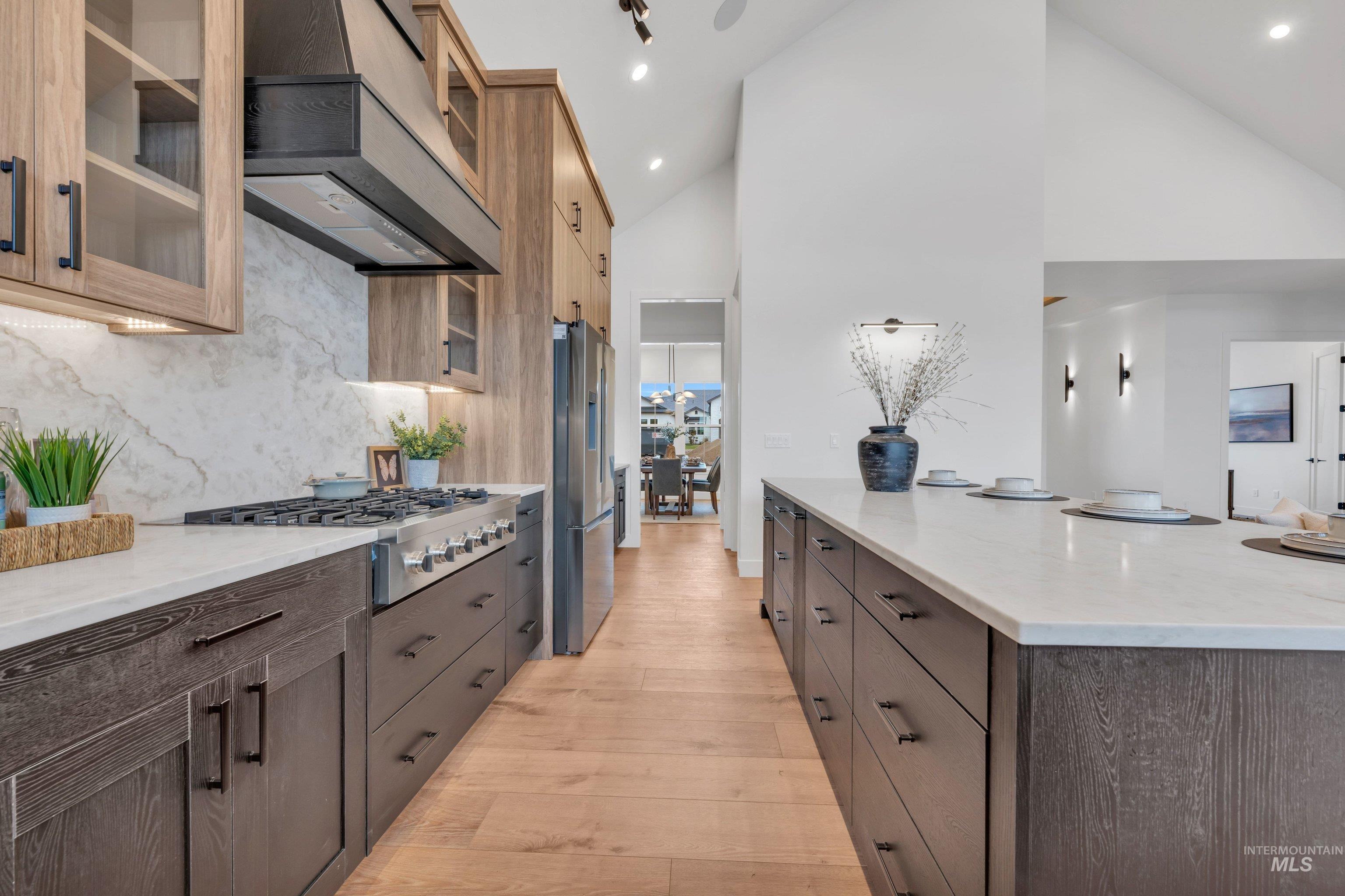 24871 Ardmore Court Caldwell, ID 83607 - Photo 15 of 44 Kitchen featuring glass fronted cabinets, ventilation hood, light stone counters, light wood-style flooring, and stainless steel appliances