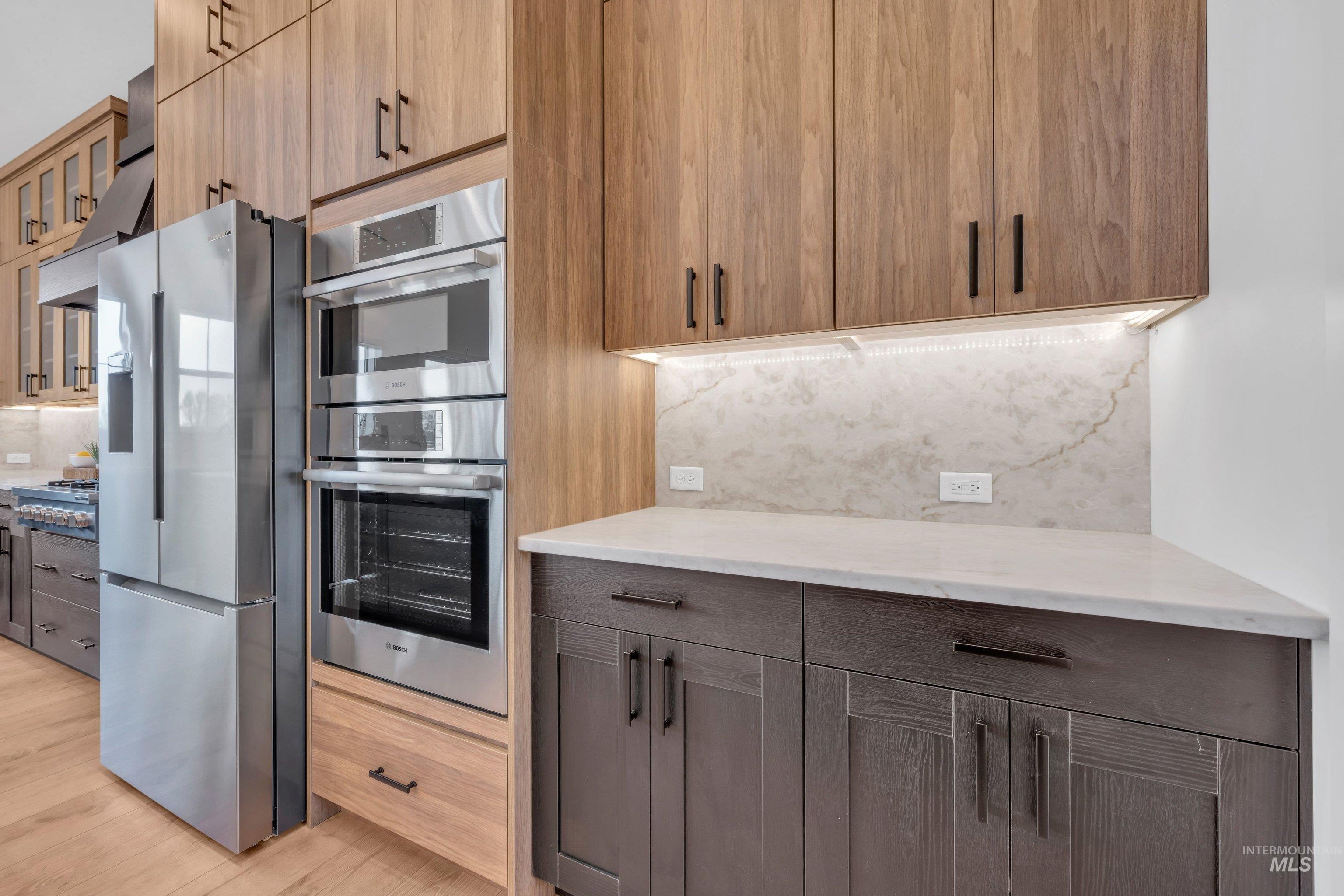 24871 Ardmore Court Caldwell, ID 83607 - Photo 16 of 44 Kitchen with stainless steel appliances, backsplash, light stone counters, glass fronted cabinets, and modern cabinets