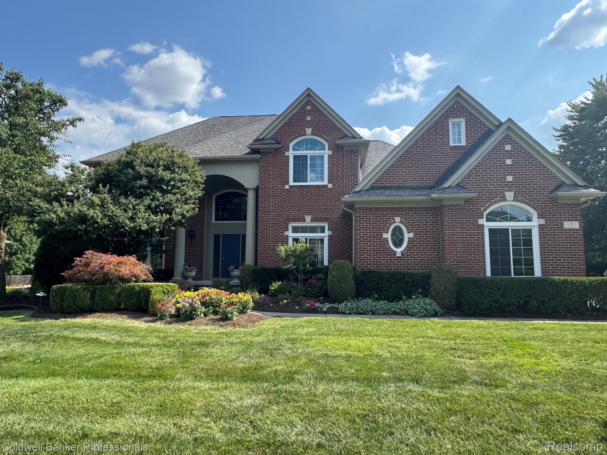 171 Millstone Road Troy, MI 48084 - Photo 42 of 43 Brick Colonial residence showcasing a gabled roofline with multiple peaks, arched entryway with dark wood doors, and a prominent circular window detail