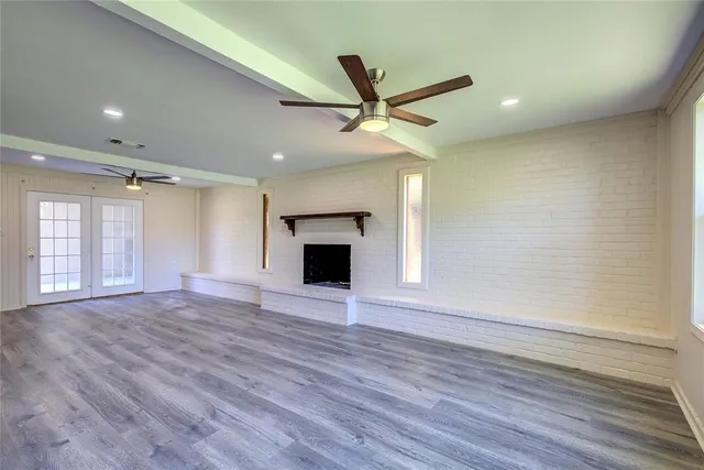 an empty room with wooden floor a ceiling fan a fireplace and windows