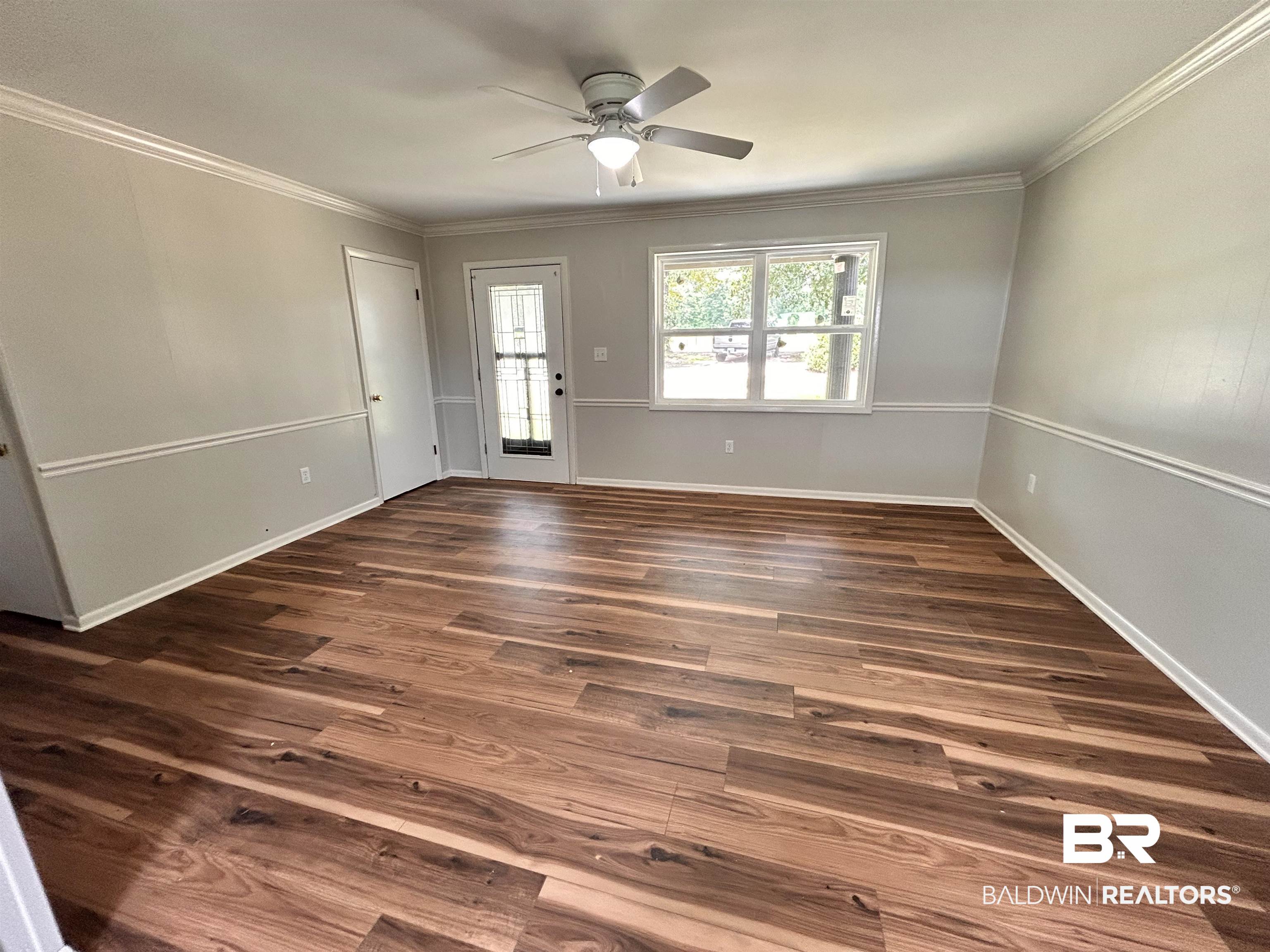 7870 Bradley Road Brewton, AL 36426 - Photo 3 of 8 Spacious room featuring wood-finish flooring, two-tone walls with chair rail molding, and crown molding