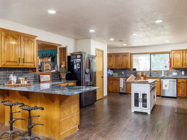 a kitchen with stainless steel appliances granite countertop a refrigerator a sink dishwasher a stove and a dining table with wooden floor