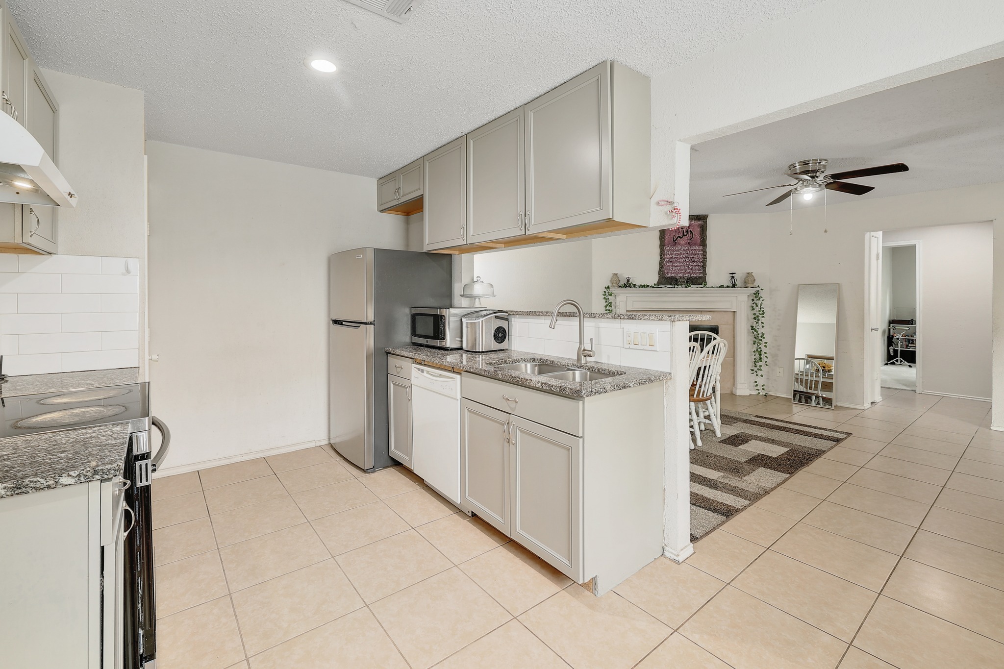 9901 Parliament House Road Austin, TX 78729 - Photo 20 of 40 Kitchen with light stone counters, a ceiling fan, light tile patterned flooring, a peninsula, and a textured ceiling
