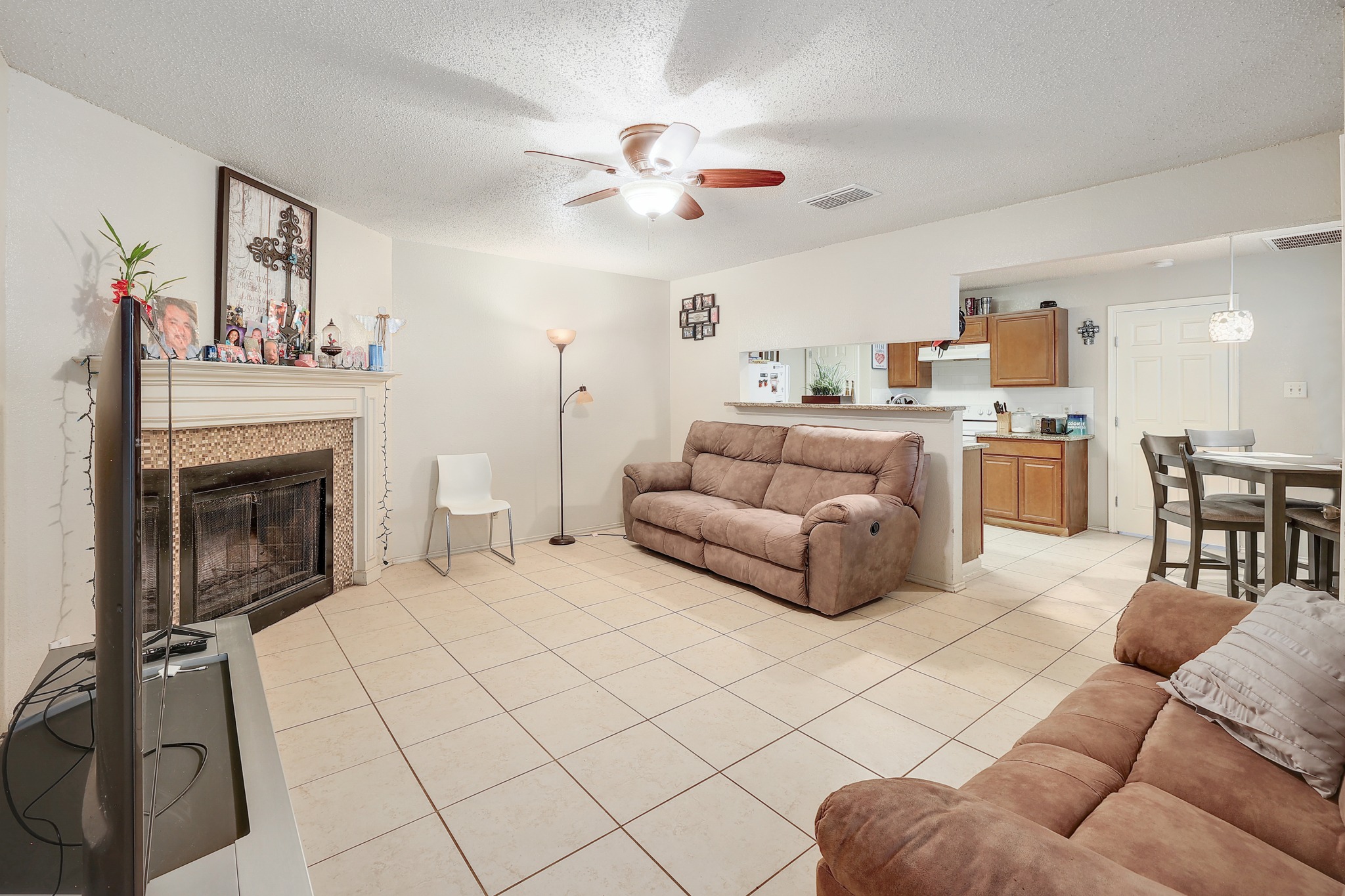 9901 Parliament House Road Austin, TX 78729 - Photo 7 of 40 Living area with ceiling fan, a textured ceiling, light tile patterned floors, and a tile fireplace