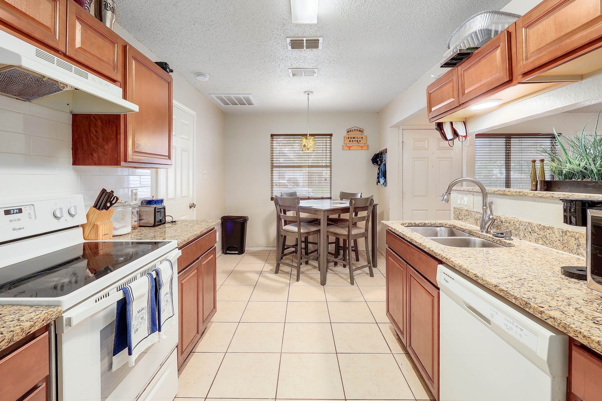 9901 Parliament House Road Austin, TX 78729 - Photo 8 of 40 Kitchen with white appliances, light stone counters, a textured ceiling, wood finish cabinets, and decorative light fixtures