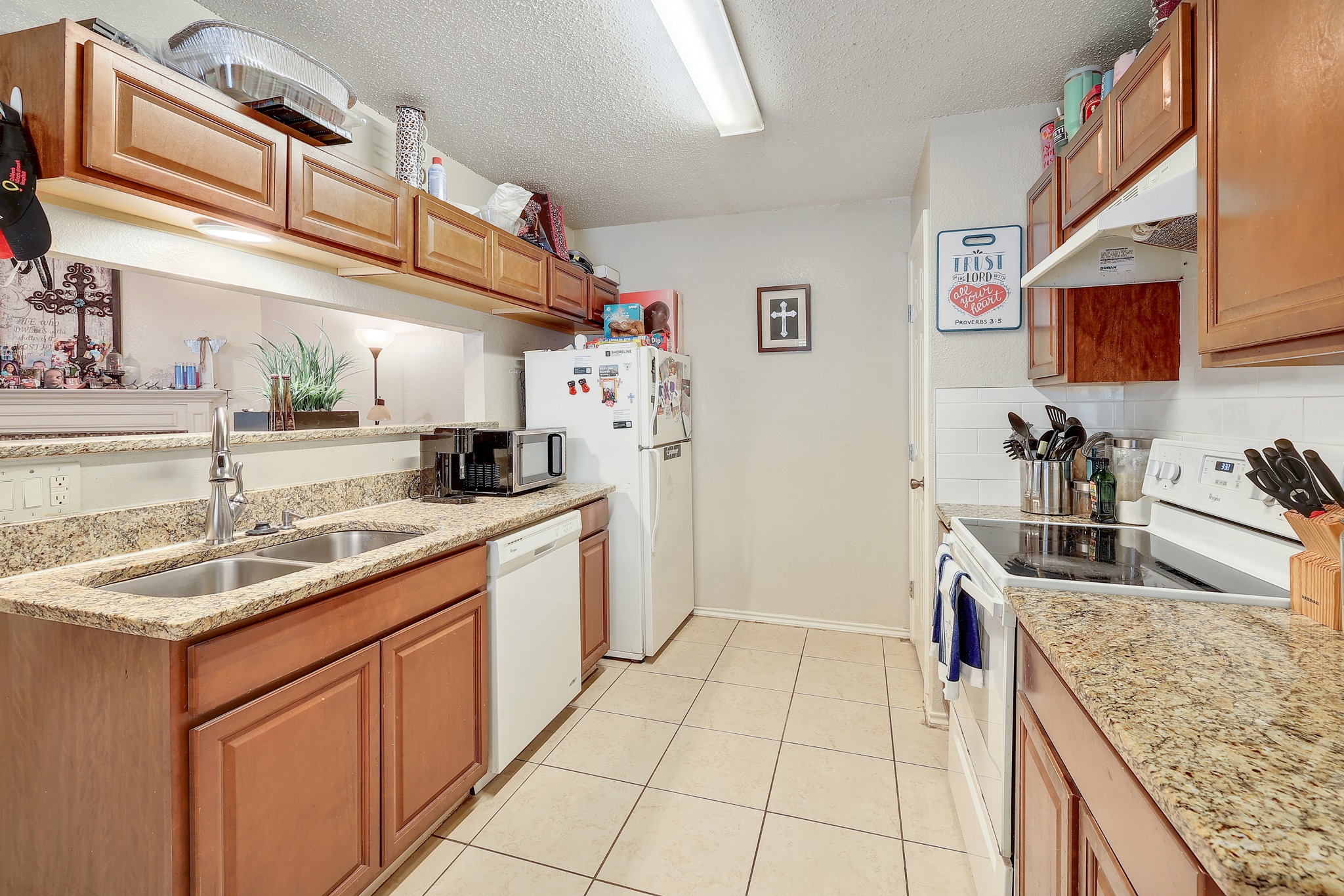 9901 Parliament House Road Austin, TX 78729 - Photo 9 of 40 Kitchen with white appliances, light stone countertops, a textured ceiling, wood finish cabinets, and light tile patterned floors