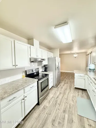 a large kitchen with granite countertop a stove top oven a sink dishwasher and white cabinets with wooden floor