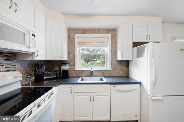 a kitchen with granite countertop white cabinets white appliances a sink and a window