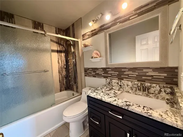 a bathroom with a granite countertop sink a toilet a mirror and shower