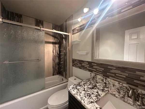 a bathroom with a granite countertop bathtub shower sink and toilet