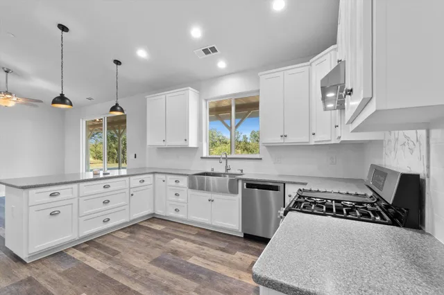 a kitchen with granite countertop a stove a sink a refrigerator and white cabinets with wooden floor