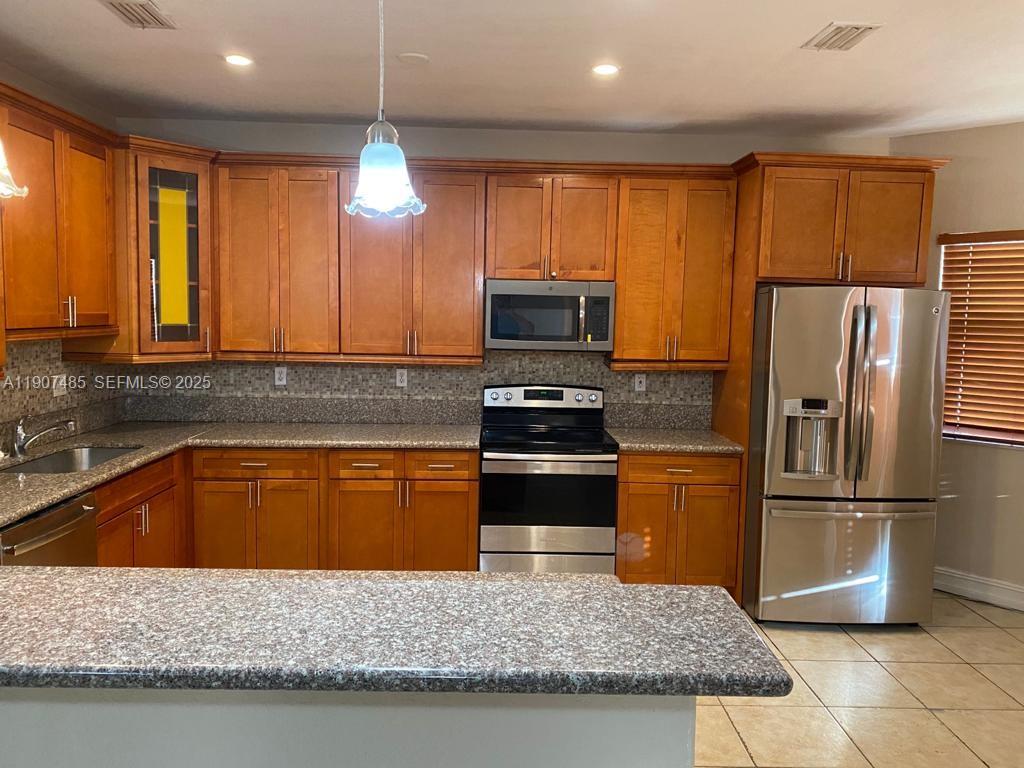 13426 Southwest 177th Terrace Miami, FL 33177 - Photo 7 of 36 a kitchen with stainless steel appliances granite countertop a refrigerator a stove a sink dishwasher a oven with large countertops bookshelf and wooden cabinets