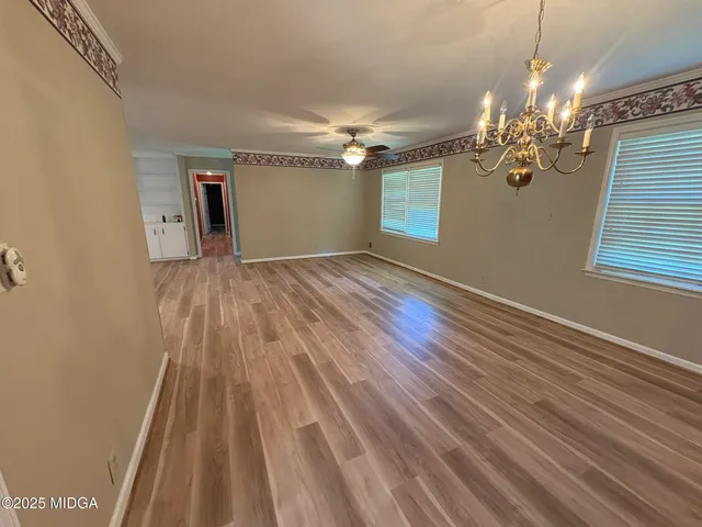 a view of an empty room with chandelier fan and wooden floor