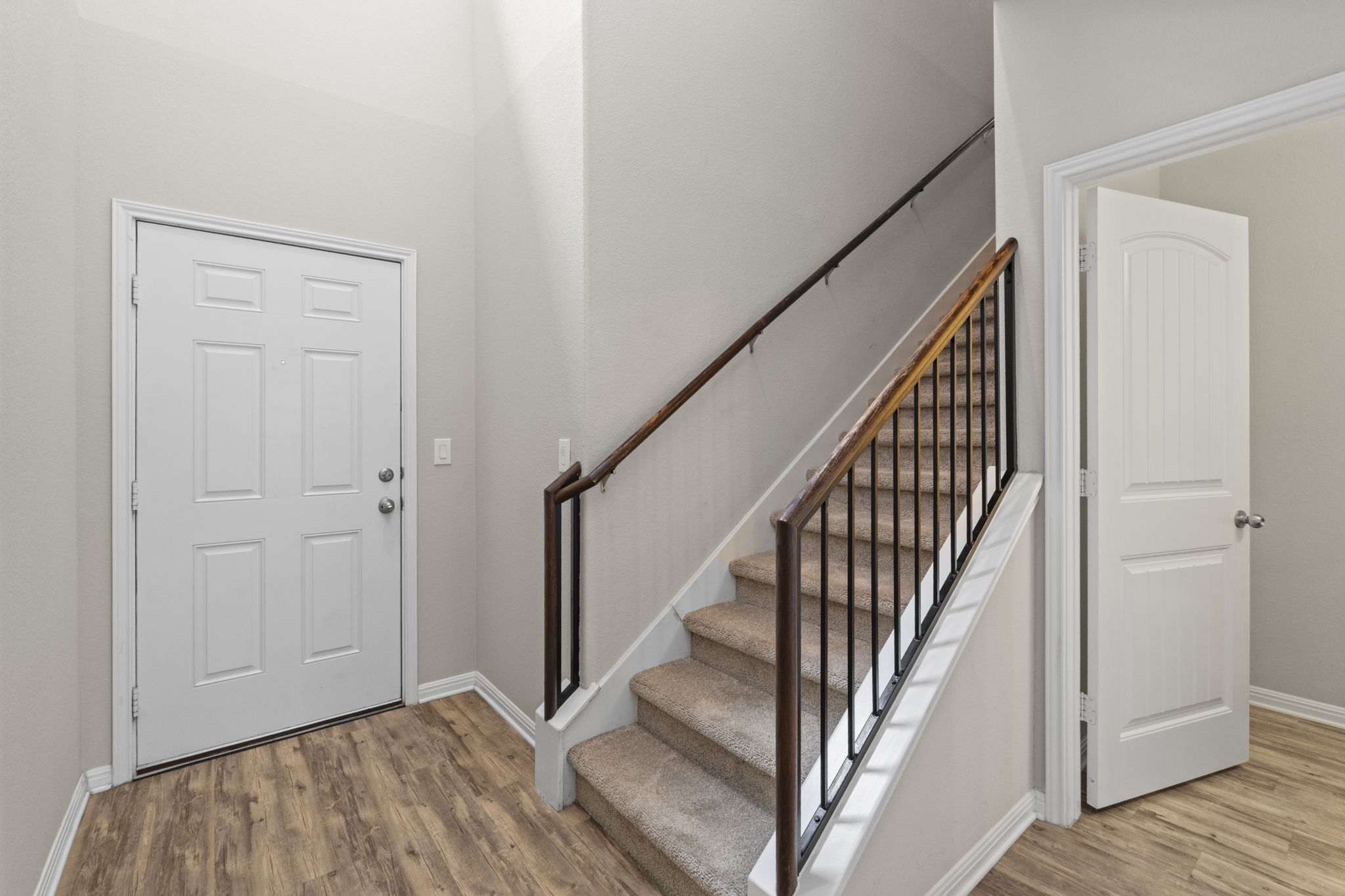 516 East Slaughter Lane, Unit 2001 Austin, TX 78744 - Photo 10 of 31 Entryway featuring wood-look flooring, a white paneled door, and a staircase with carpeted treads and a dark wood handrail with black balusters