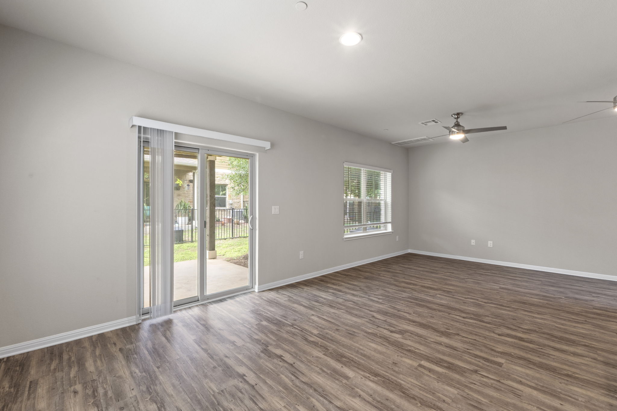516 East Slaughter Lane, Unit 2001 Austin, TX 78744 - Photo 14 of 31 Spacious room featuring wood-look flooring, a ceiling fan, and a large sliding glass door opening to an outdoor patio with a fenced area