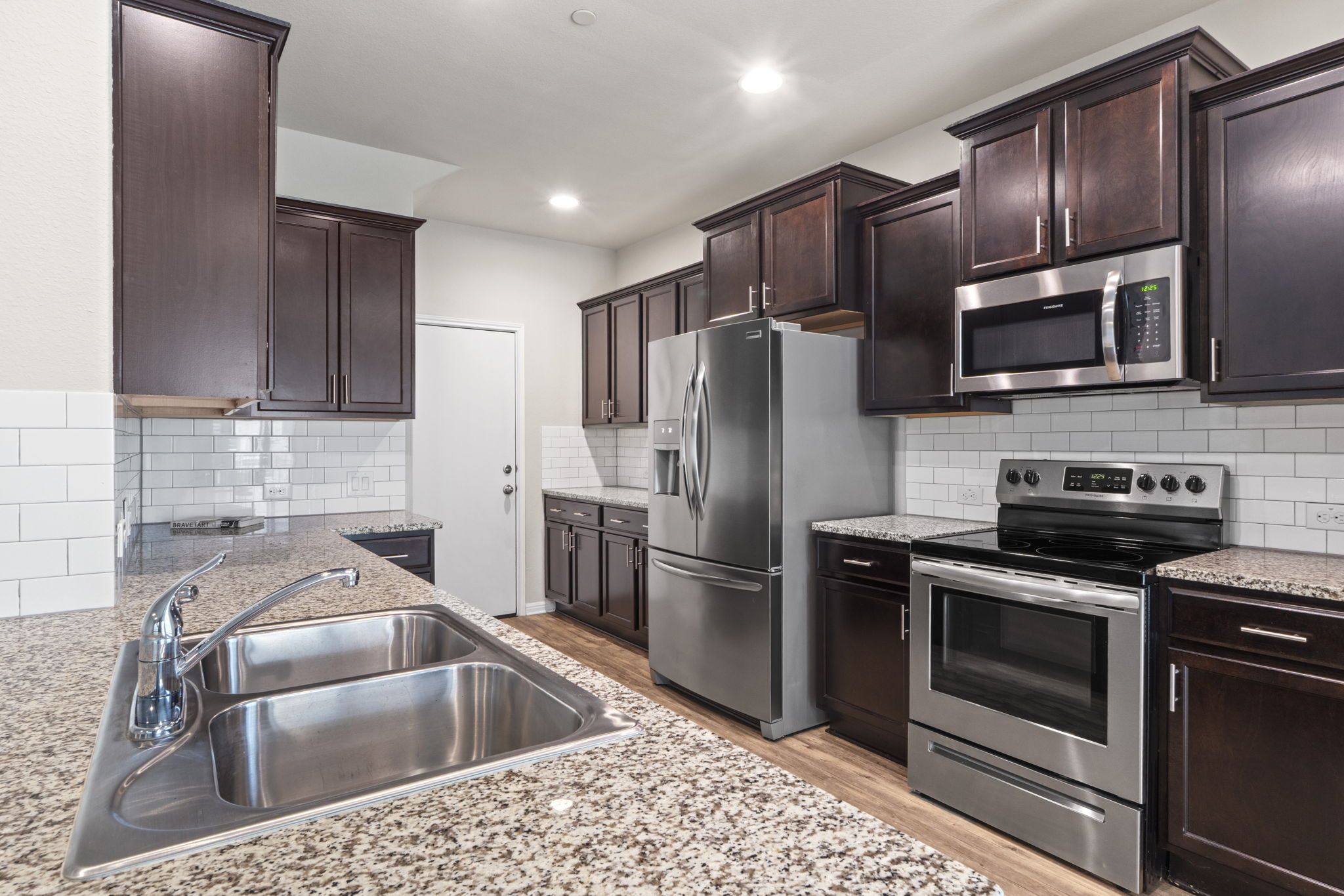 516 East Slaughter Lane, Unit 2001 Austin, TX 78744 - Photo 17 of 31 The property features a kitchen with dark wood cabinetry, granite countertops, a stainless steel double basin sink with a chrome faucet, stainless steel appliances, and a white subway tile backsplash