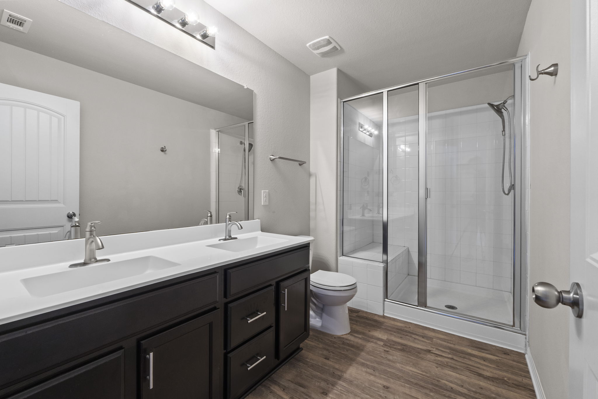 516 East Slaughter Lane, Unit 2001 Austin, TX 78744 - Photo 6 of 31 Bathroom featuring a dual vanity with dark wood cabinetry, a large mirror, a shower with a clear glass enclosure, and wood-look flooring