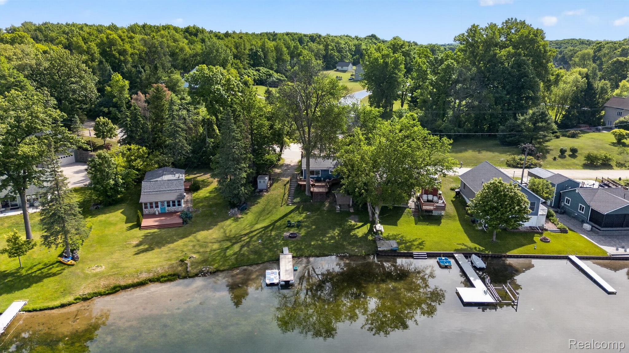 1717 Triangle Lake Road Howell, MI 48843 - Photo 24 of 58 Lakeside property featuring a boat dock, expansive grassy areas, mature trees, and a sandy shoreline