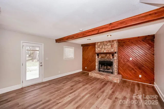 an empty room with wooden floor fireplace and windows