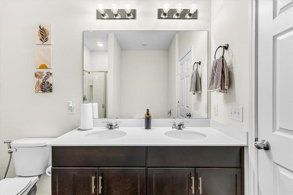1201 Timberhurst Trail Fort Worth, TX 76131 - Photo 20 of 40 Dual-sink vanity featuring a dark wood-finish cabinet base with brushed metal hardware, white quartz countertop, and chrome faucets