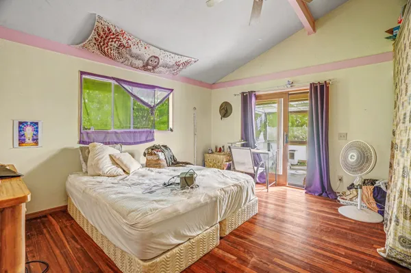 a bedroom with a bed a mirror and a large window with wooden floor