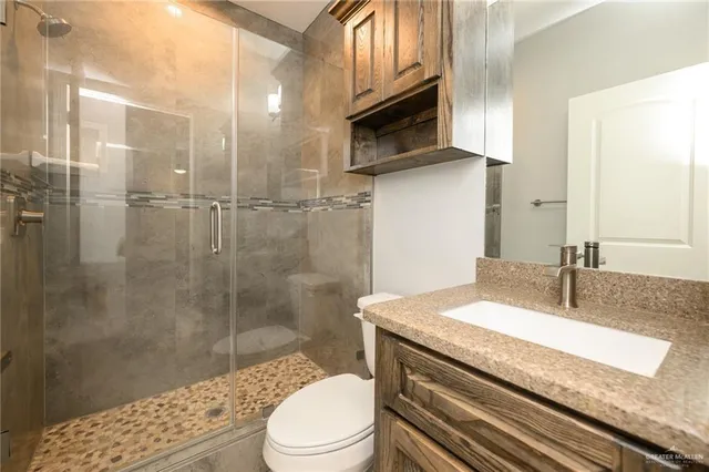 a bathroom with a granite countertop sink a toilet a mirror and shower