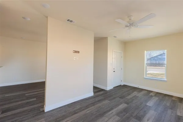 an empty room with wooden floor fan and windows
