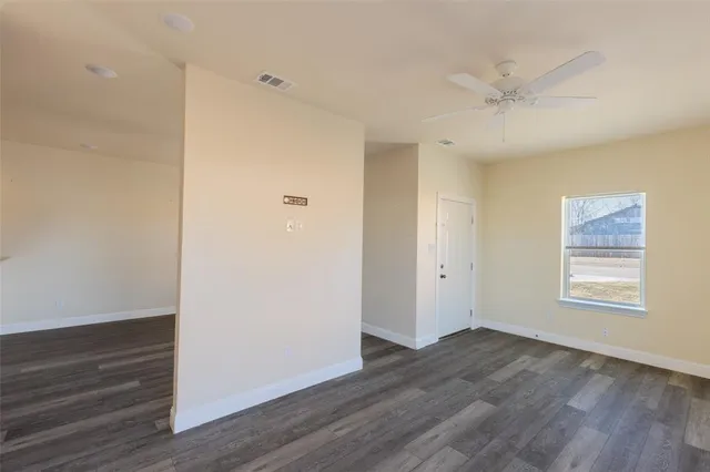 an empty room with wooden floor fan and windows