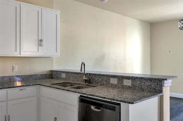 a kitchen with granite countertop a sink dishwasher a stove and white cabinets