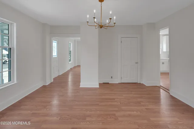 an empty room with wooden floor chandelier and windows