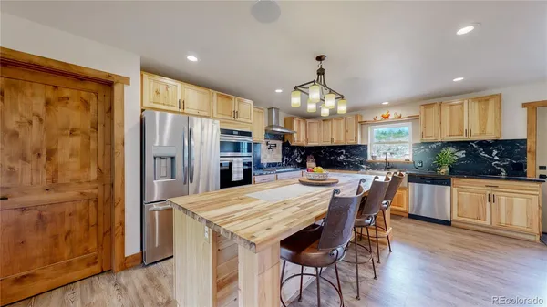 a kitchen with stainless steel appliances kitchen island granite countertop a refrigerator a stove a sink a dining table and chairs with wooden floor