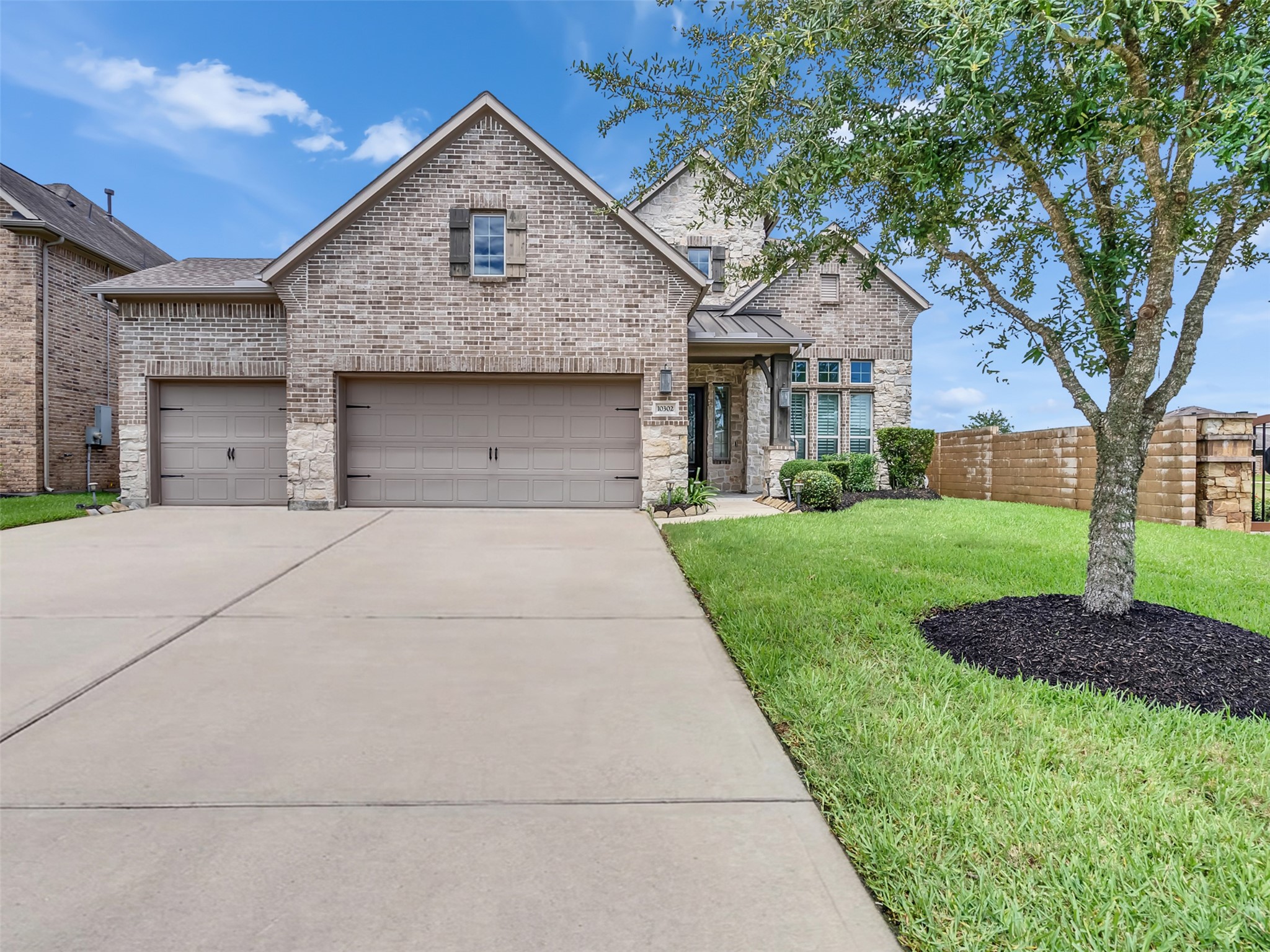 Charming two-story brick and stone home with a well-maintained front yard, attached 3-car garage, and welcoming entryway.