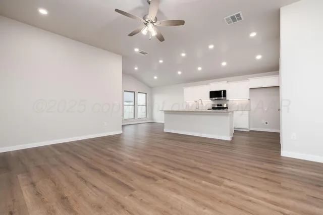 an empty room with wooden floor a ceiling fan and kitchen view