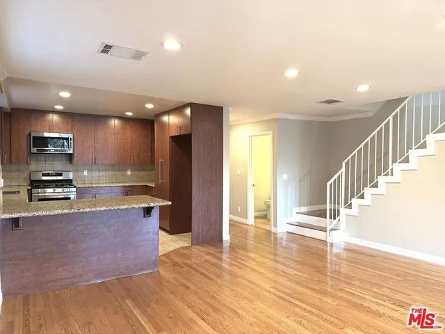 a open kitchen with stainless steel appliances granite countertop a refrigerator a sink a stove and oven with wooden floor