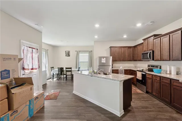a living room with stainless steel appliances kitchen island granite countertop a table chairs sink and cabinets