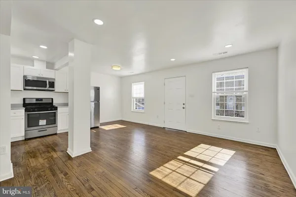 an empty room with wooden floor and kitchen view