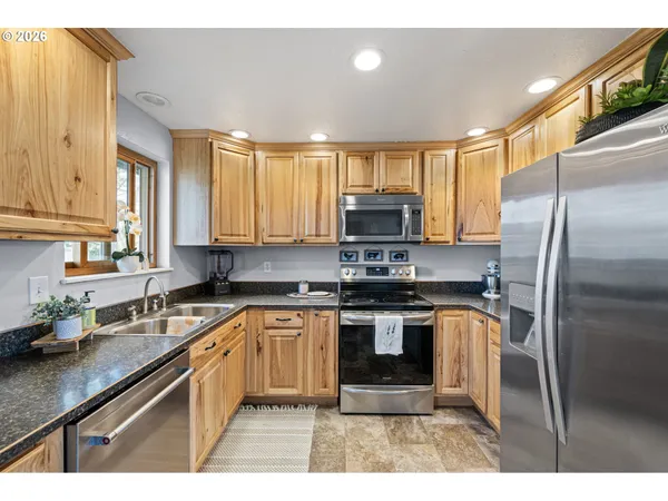 a kitchen with stainless steel appliances granite countertop a sink a stove a refrigerator cabinets and a window