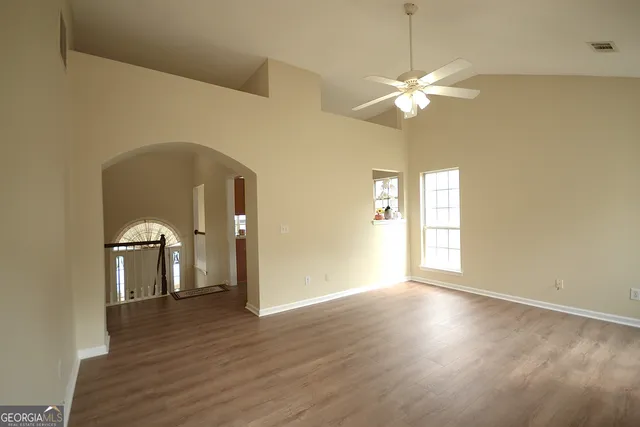 a view of a room with wooden floor a ceiling fan and windows