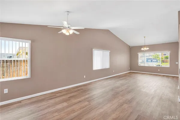 an empty room with wooden floor ceiling fan and windows