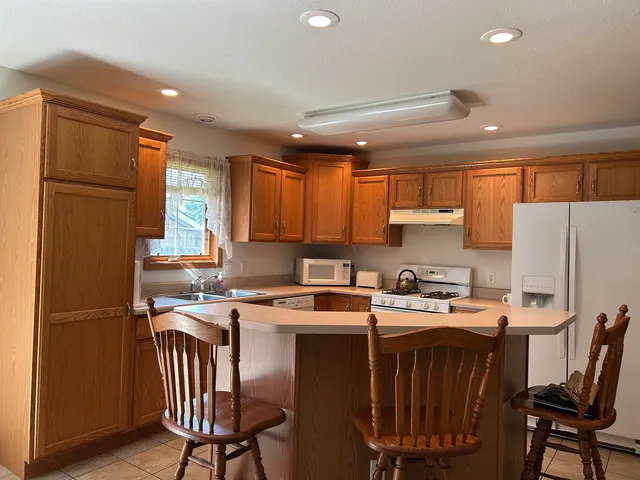 a kitchen with stainless steel appliances granite countertop a refrigerator a stove a sink dishwasher a dining table and chairs with wooden floor
