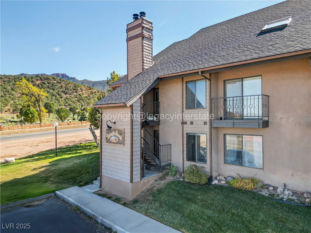 390 East 300 South, Unit 3A Parowan, UT 84761 - Photo 1 of 25 Back of property with a yard, a shingled roof, a chimney, stucco siding, and a mountain view