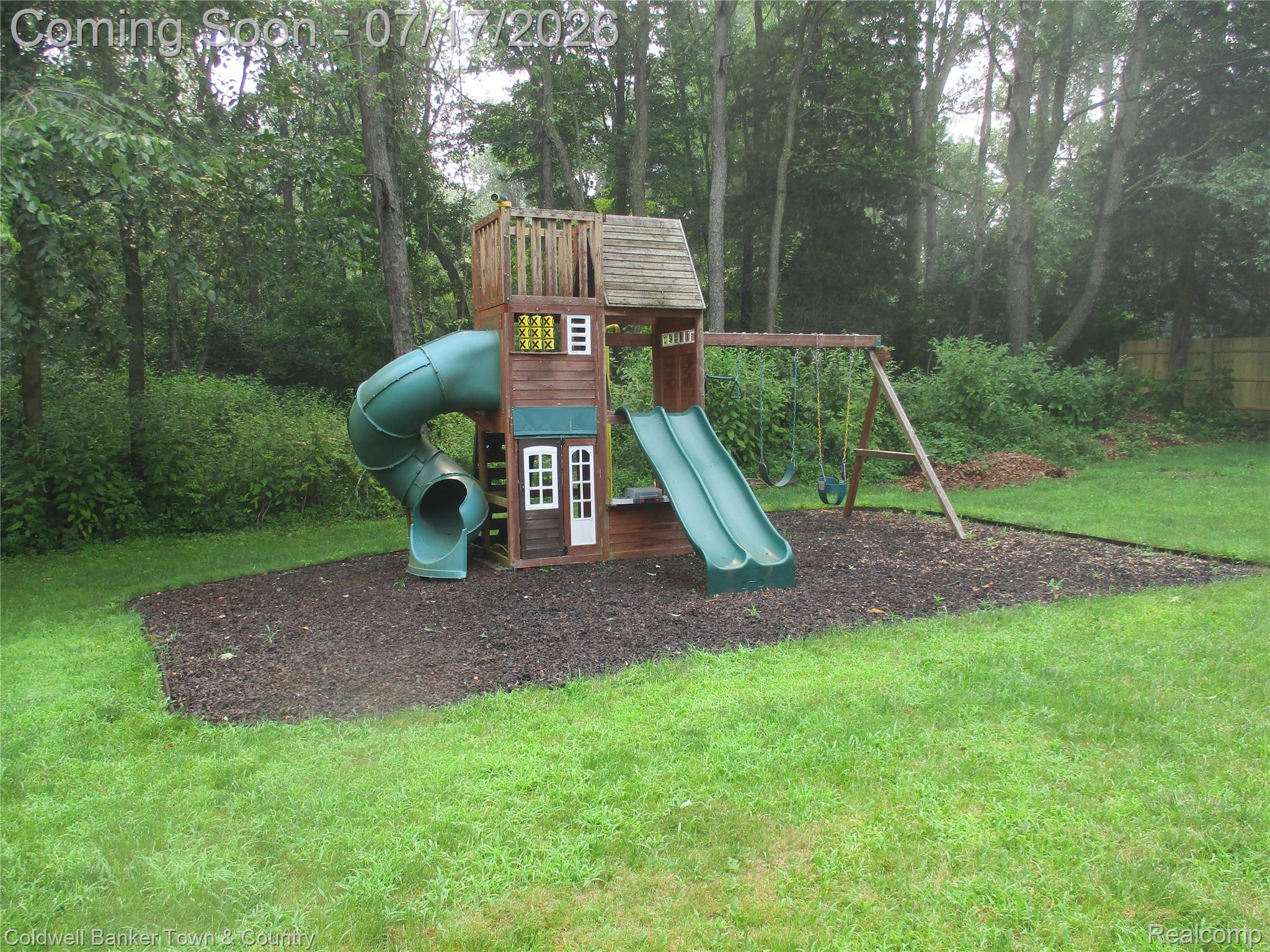 1996 Triangle Lake Road Howell, MI 48843 - Photo 31 of 32 Backyard featuring a multi-level wooden playset with two slides, a swing set, and a surrounding rubber chip surface