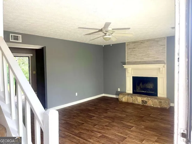 a view of a livingroom with a fireplace a ceiling fan and wooden floor