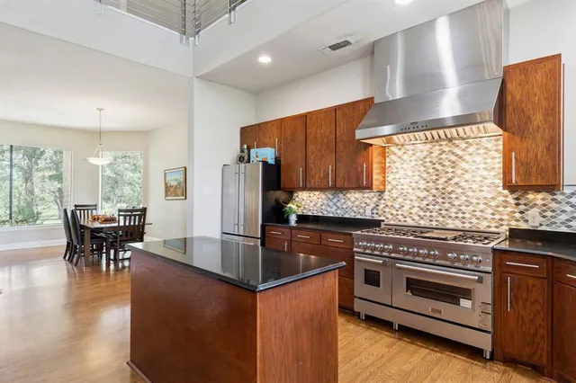 a kitchen with stainless steel appliances granite countertop a stove top oven a sink a dining table and chairs with wooden floor